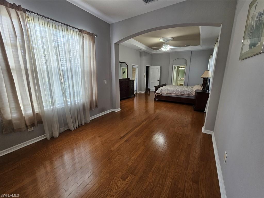 Expansive interior space featuring wood-finish flooring, an arched entryway, and a tray ceiling with a ceiling fan