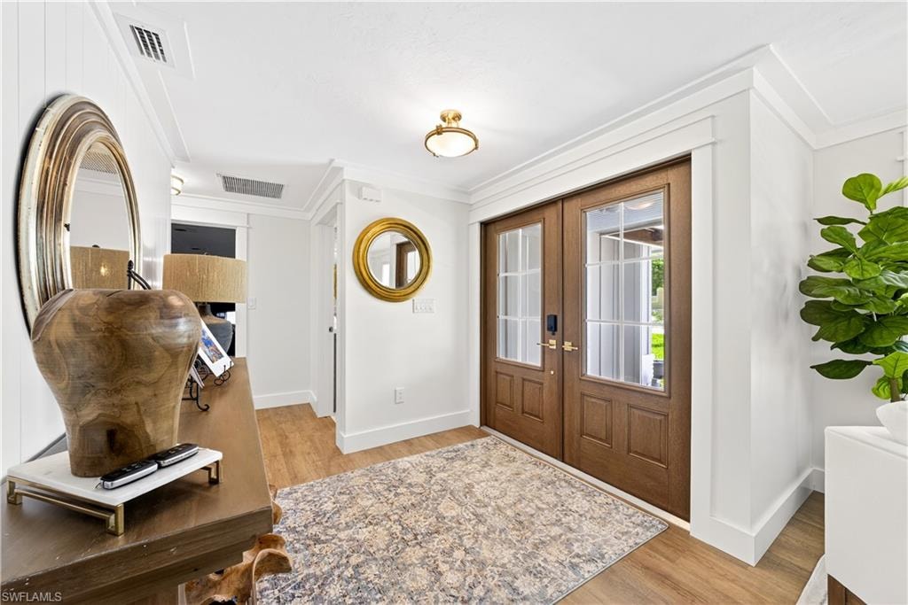 Entryway featuring double wood-paneled doors with glass inserts, wood-finish flooring, and crown molding
