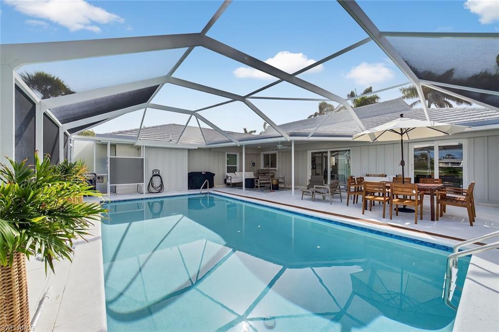 Screened pool enclosure featuring a large rectangular pool with integrated steps, a spacious paved patio, and multiple sliding glass door entries to the main residence