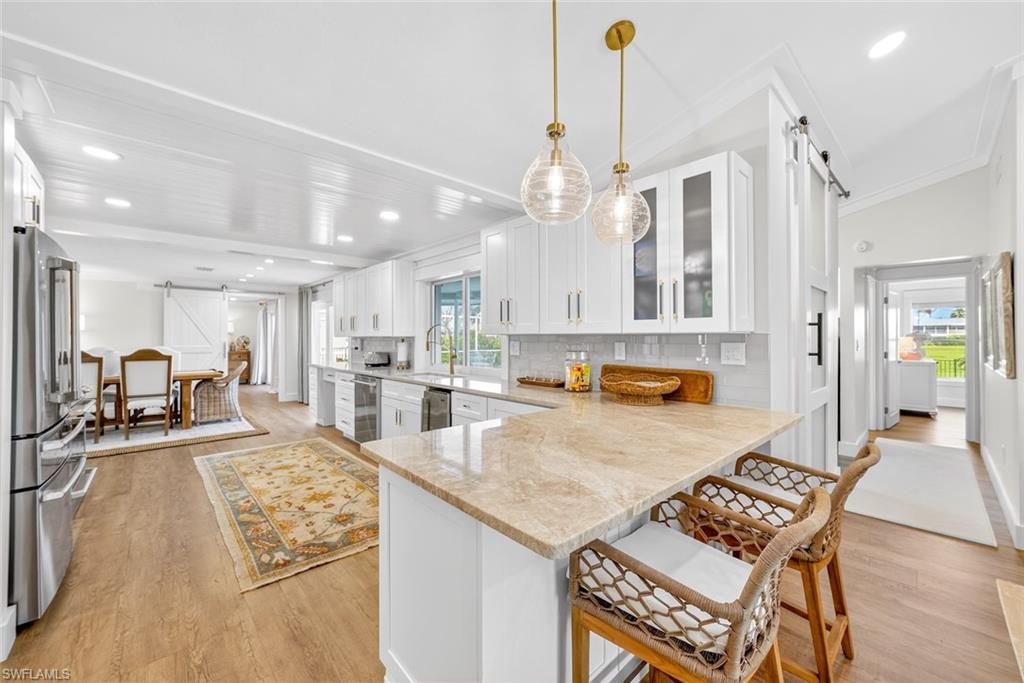 Open-concept kitchen featuring an island with stone countertop, white shaker cabinetry, stainless steel appliances, and wood-finish flooring
