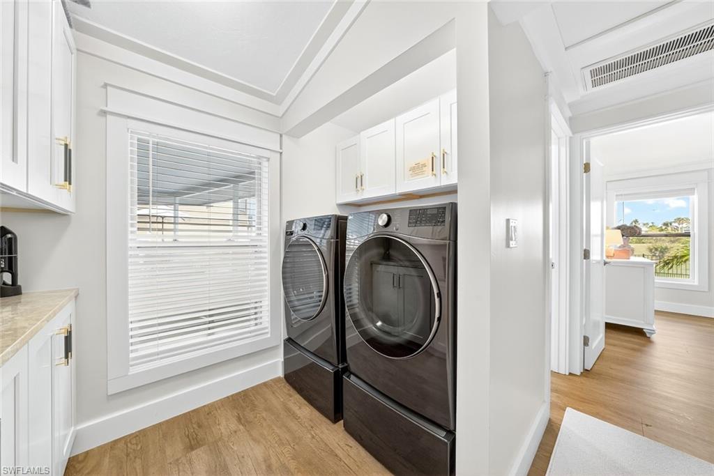 Dedicated laundry area featuring wood-finish flooring, white cabinetry with gold-tone hardware, and a window with horizontal blinds