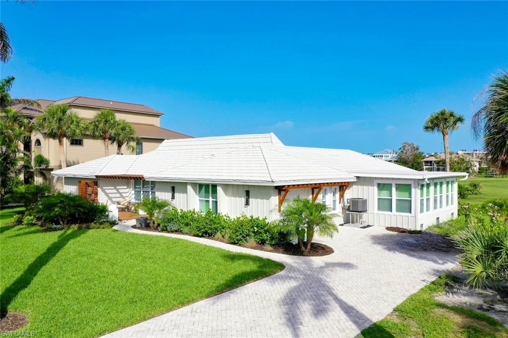 White exterior residence featuring a bright white roof, a sunroom with multiple windows, a paver driveway, and a well-manicured lawn with mature landscaping