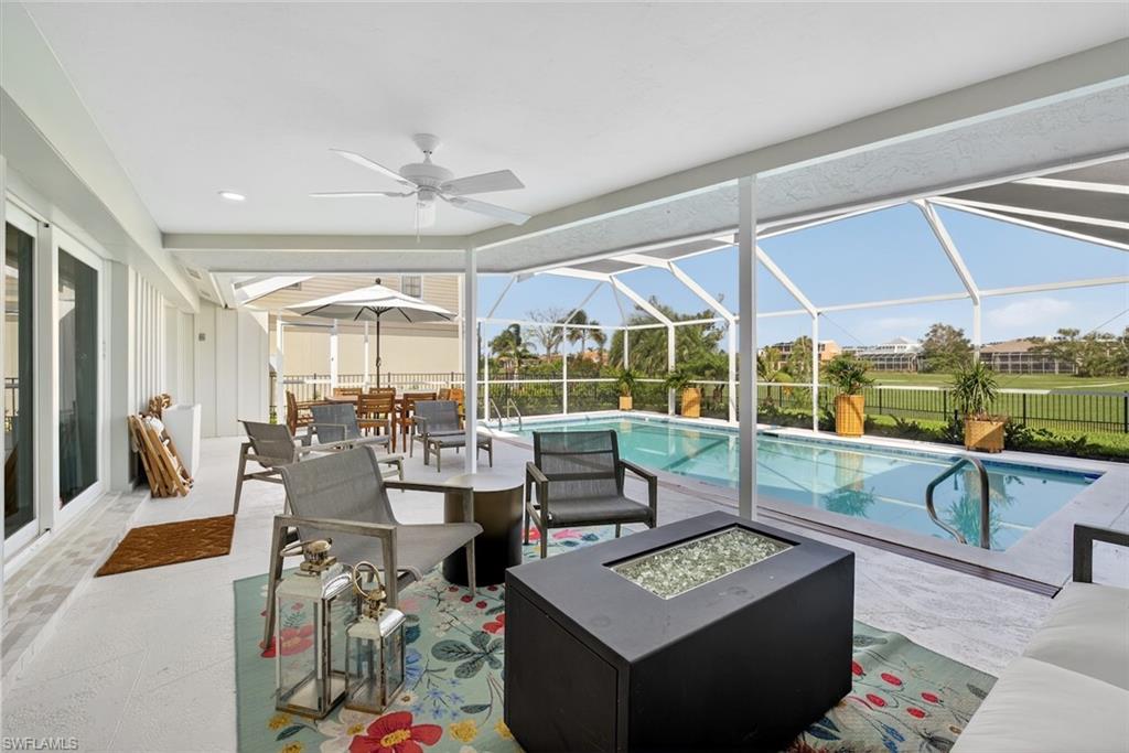 Expansive screened lanai featuring a ceiling fan, a rectangular swimming pool with integrated steps, and a decorative fire pit