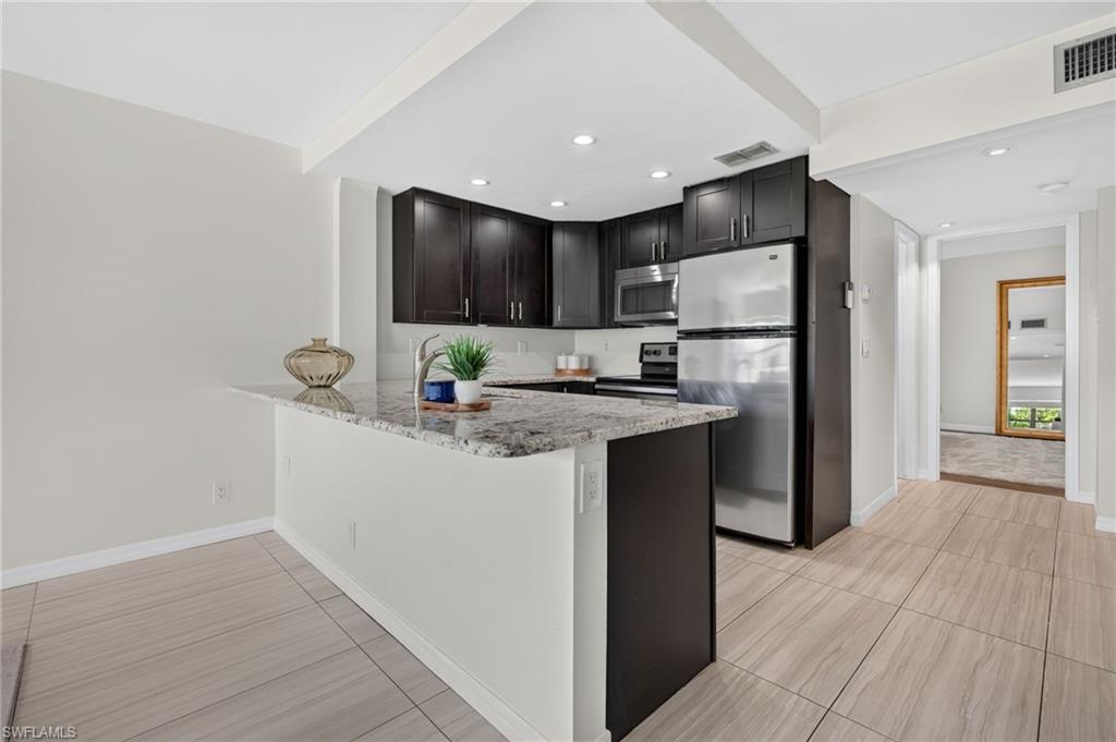 Kitchen featuring dark wood-finish cabinetry, stainless steel appliances, recessed lighting, and a peninsula with a light-toned countertop