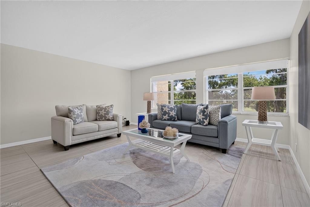 Spacious living area featuring light-toned wall finishes, expansive windows, and wood-finish tile flooring