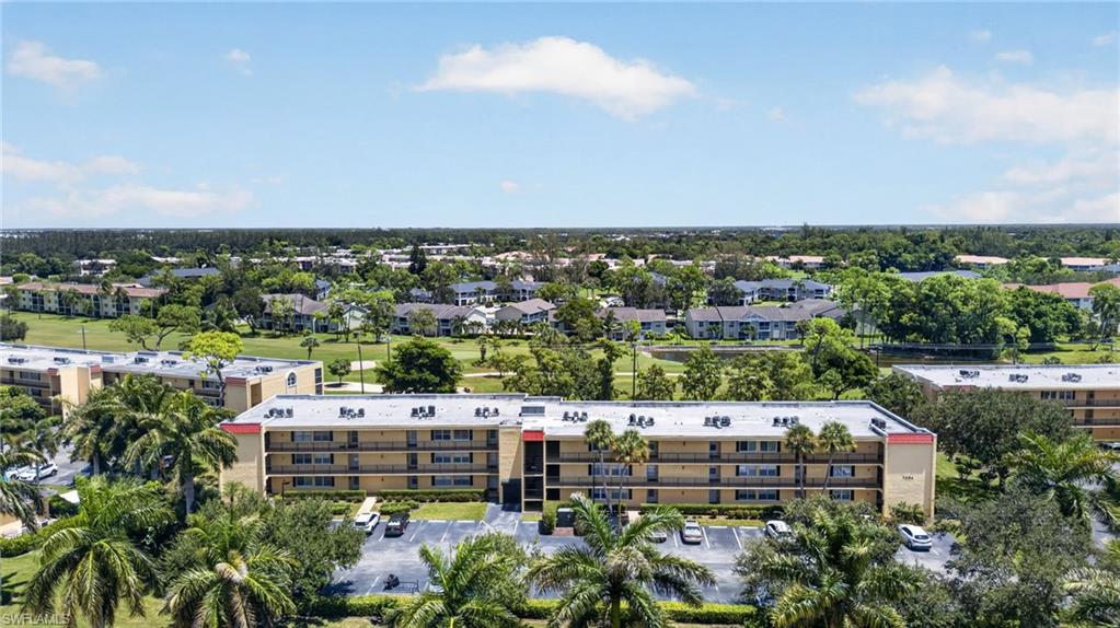 Multi-story building featuring balconies, mature palm trees, and a surrounding paved parking area