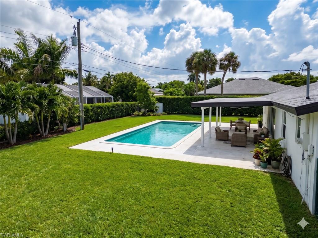 Expansive backyard featuring a rectangular swimming pool with a white coping, a covered patio area with a dark roof and white support columns, and a large manicured lawn