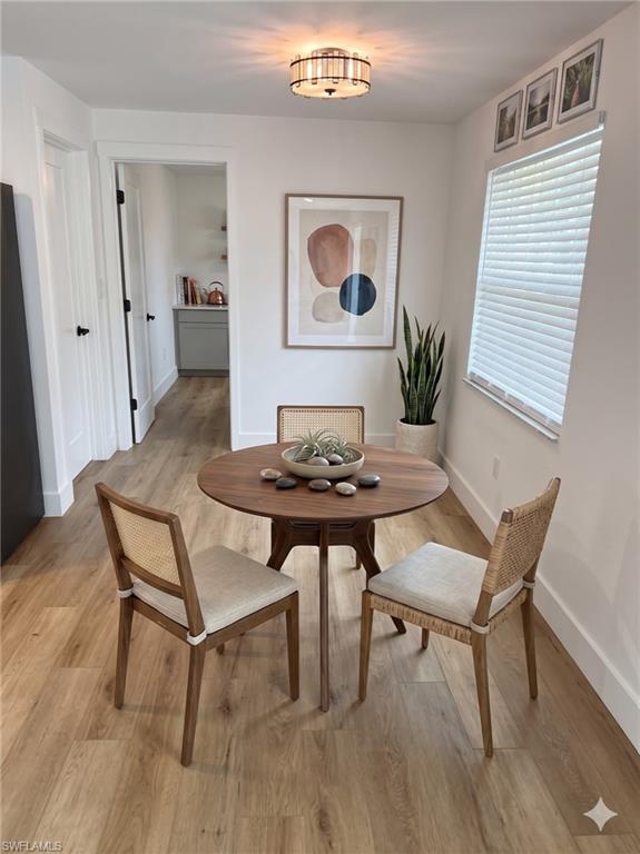 Dining area featuring wood-finish flooring, a contemporary ceiling light fixture, a window with horizontal blinds, and white baseboards
