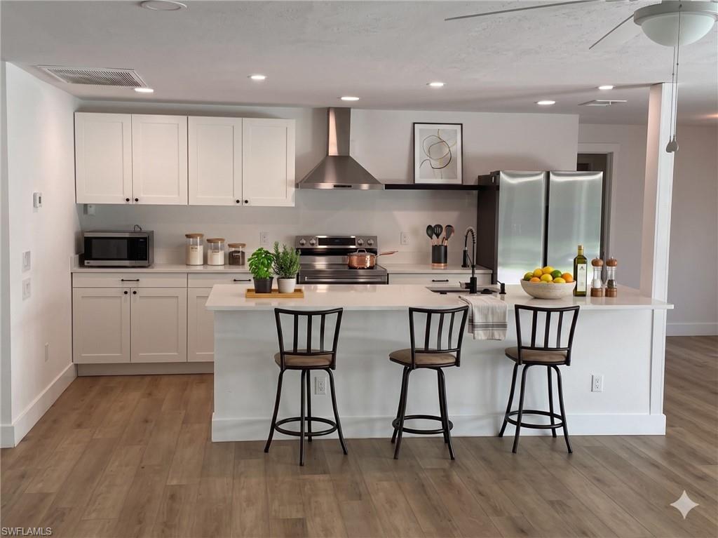 Modern kitchen featuring white shaker cabinetry, stainless steel appliances, a center island with seating, recessed lighting, and wood-finish flooring