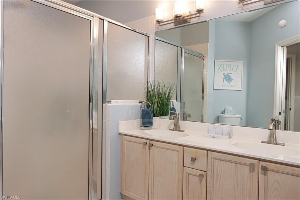 Bathroom featuring double vanity, an enclosed shower, and toilet