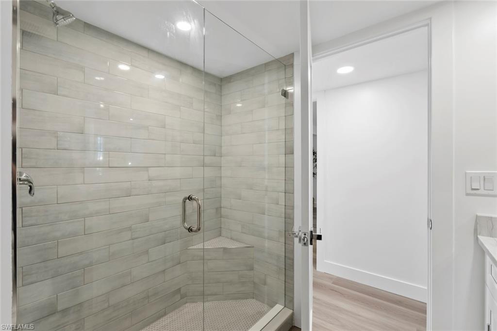 Walk-in shower with clear glass enclosure, light-toned horizontal tile, a corner bench, and a rainfall showerhead