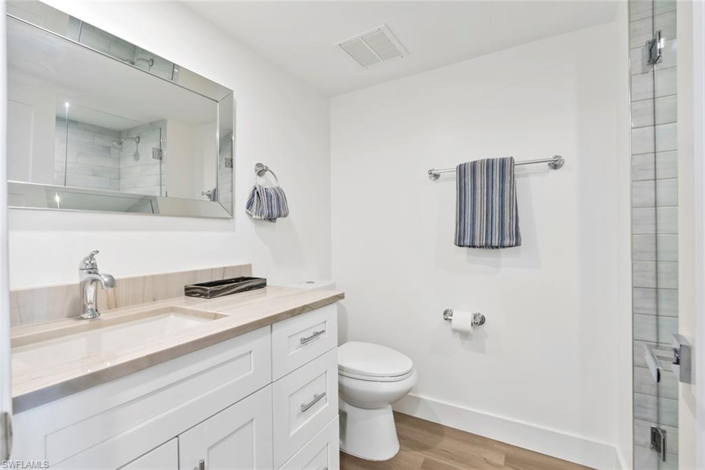 Bathroom featuring a white vanity with a light-toned countertop and integrated sink, chrome hardware, a frameless mirrored medicine cabinet, and wood-finish flooring