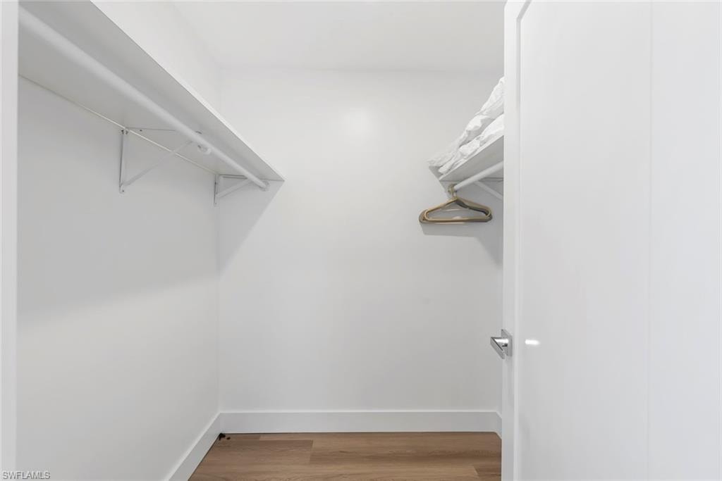 Walk-in closet featuring light wood-finish flooring, white walls, white baseboards, and built-in white shelving with hanging rods