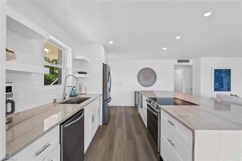 Contemporary kitchen featuring an expansive island with an integrated cooktop, white shaker-style cabinetry, stainless steel appliances, light-toned countertops, and wood-finish flooring