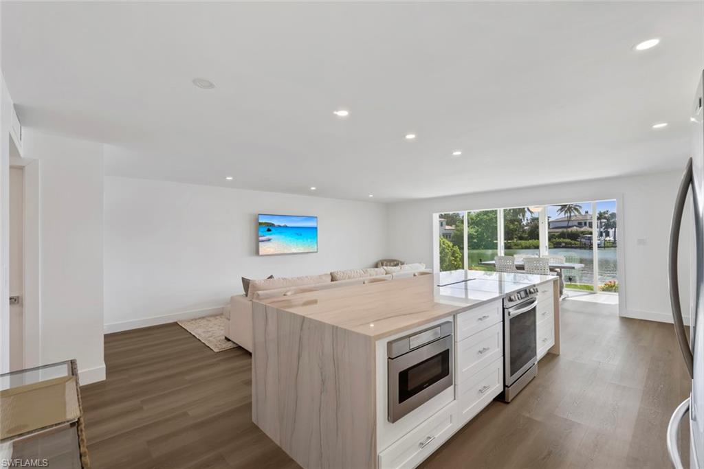 Open-concept living space featuring a modern kitchen island with waterfall countertop, integrated microwave, and stainless steel range