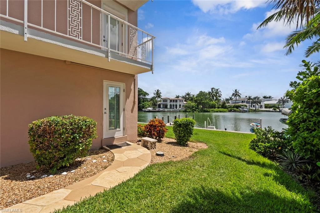Second entrance to first floor condo. Waterfront property featuring a manicured lawn, stone pathway, mature landscaping, and an upper-level balcony with decorative railing