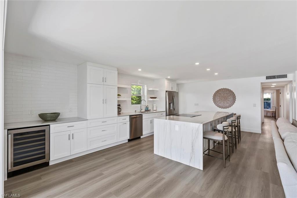 Modern kitchen featuring a waterfall-edge island with seating, stainless steel appliances, white cabinetry, and wood-finish flooring