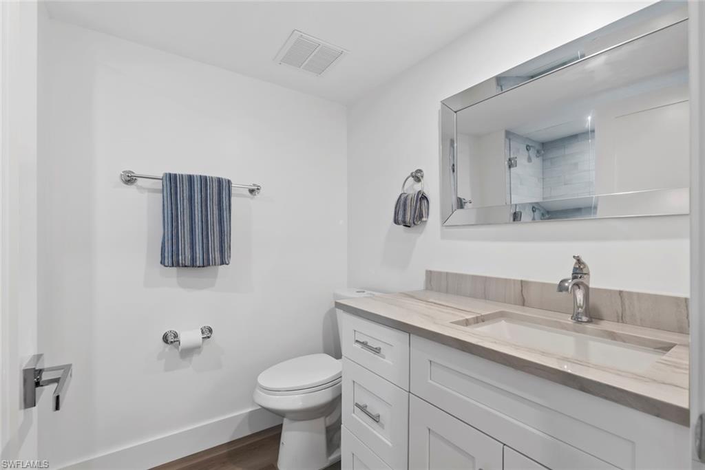 Modern bathroom featuring a white vanity with shaker-style cabinetry, a light-toned stone-finish countertop with an integrated sink, a contemporary chrome faucet, and a large frameless mirror