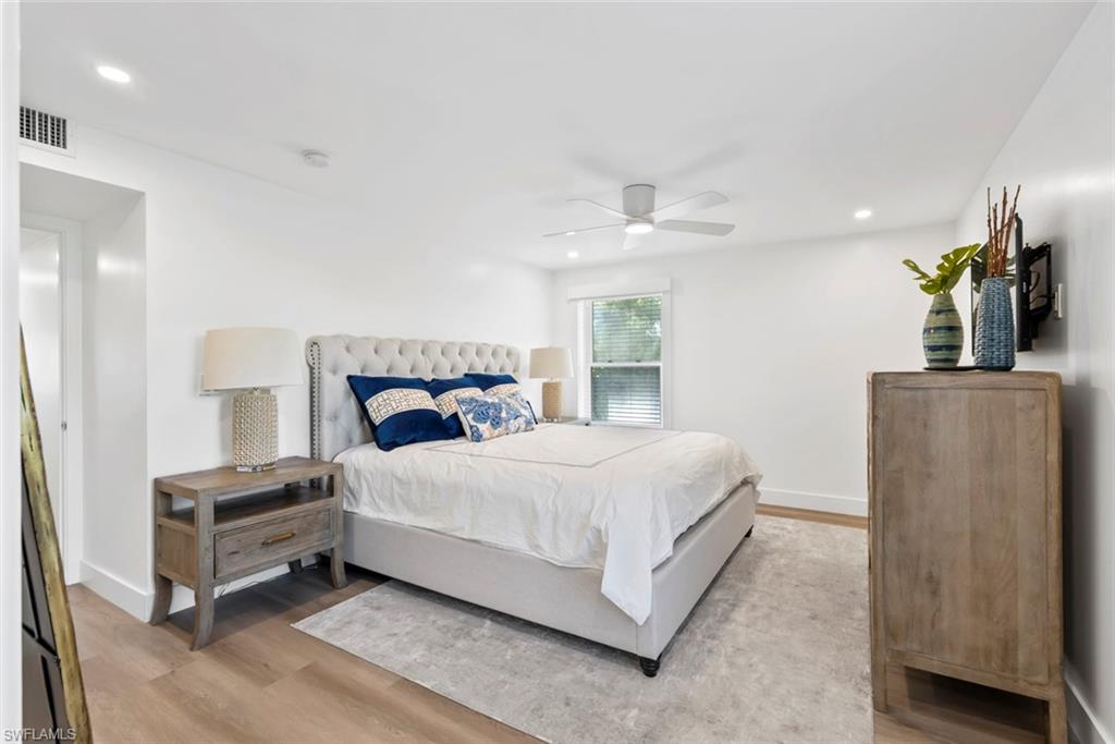 Recessed lighting illuminates this bright bedroom featuring wood-finish flooring, a ceiling fan, and a window with horizontal blinds