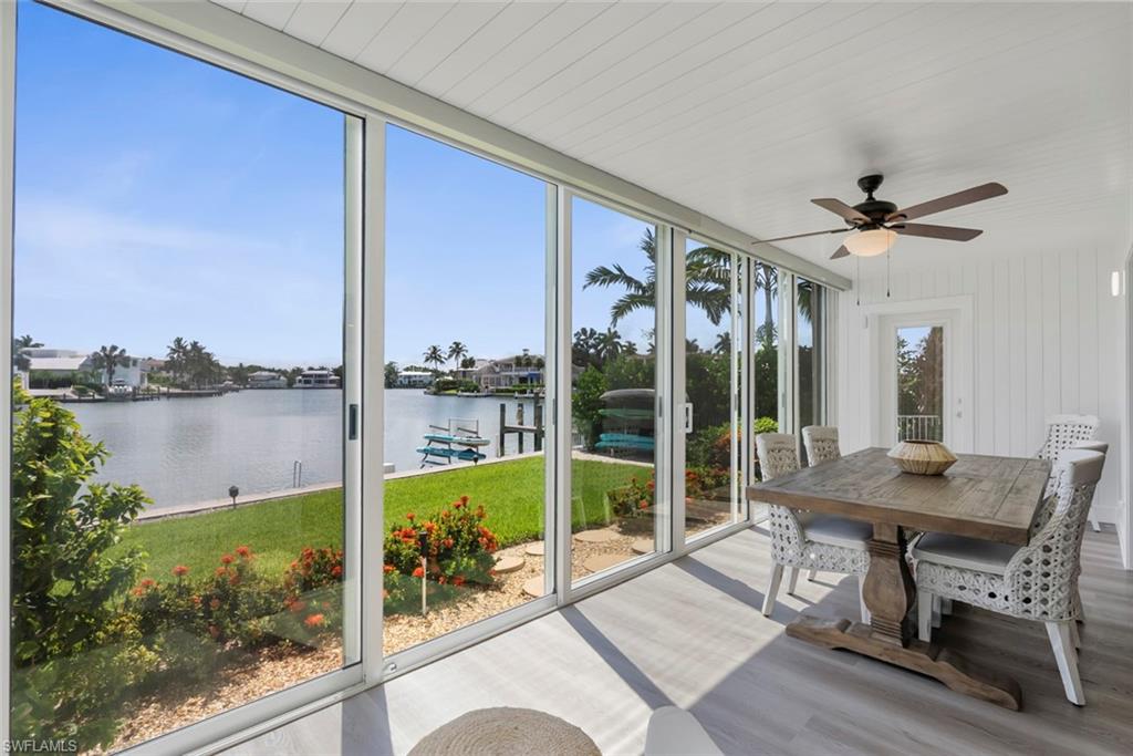 Sunroom featuring expansive sliding glass doors, water frontage, wood-finish flooring, a ceiling fan with integrated lighting, and white shiplap walls