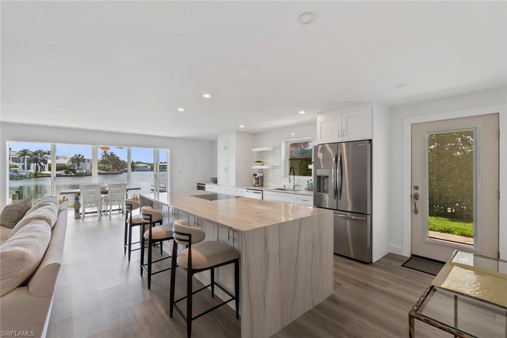 Open-concept living area featuring an expansive kitchen island with a waterfall countertop, integrated stainless steel appliances, and wood-finish flooring