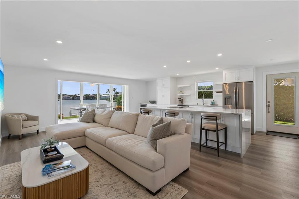 Open-concept living space featuring wood-finish flooring, recessed lighting, and a white kitchen with a peninsula island