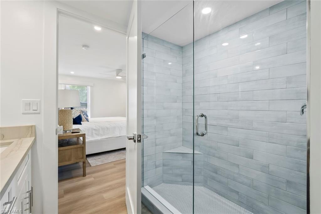 Glass-enclosed shower with subway tile surround and mosaic tile flooring, featuring a built-in corner bench and recessed lighting