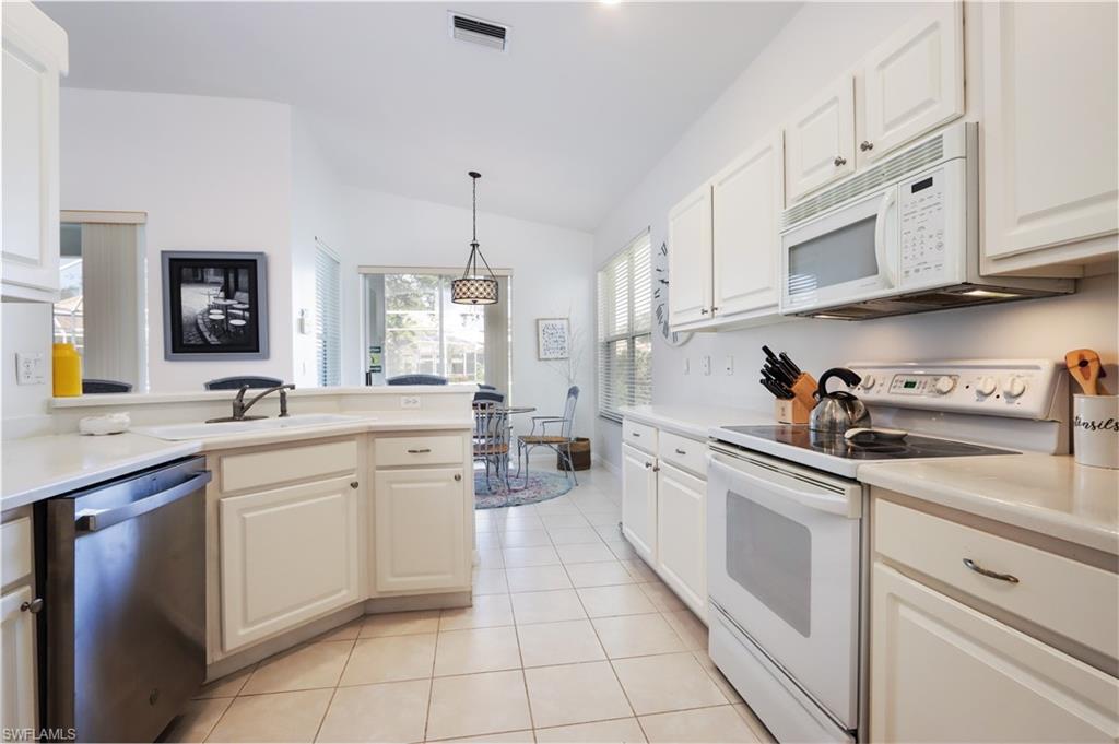 Kitchen featuring white appliances, lofted ceiling, light tile patterned floors, light countertops, and white cabinetry