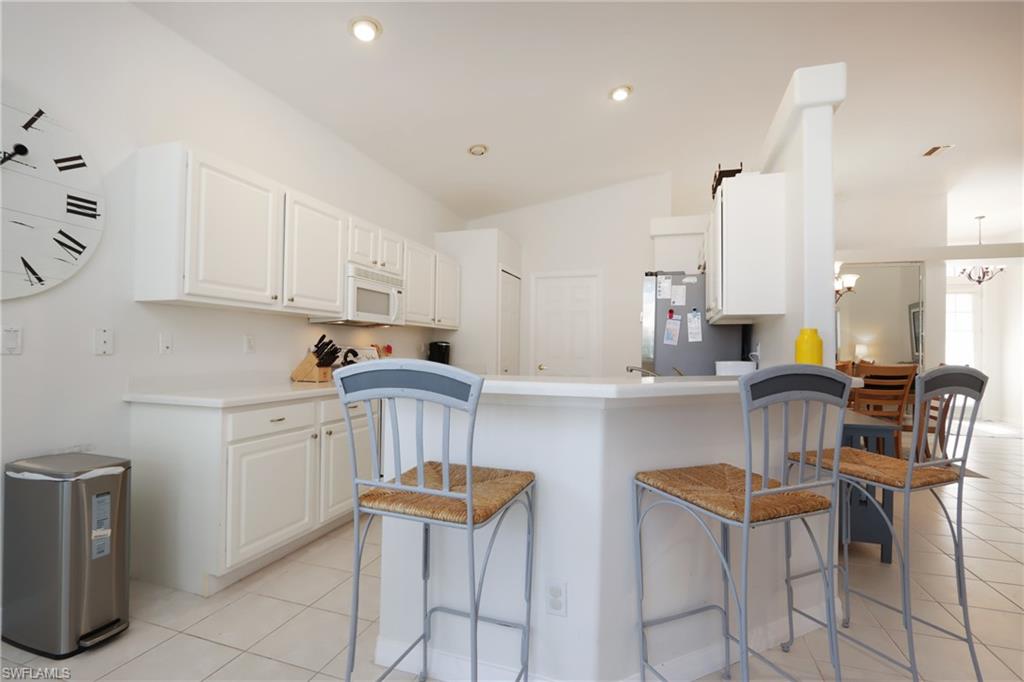 Kitchen with white microwave, a kitchen bar, light tile patterned floors, freestanding refrigerator, and recessed lighting