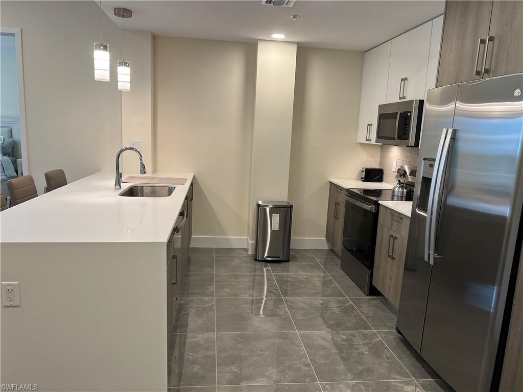 Kitchen with white cabinetry, sink, a kitchen breakfast bar, decorative light fixtures, and appliances with stainless steel finishes