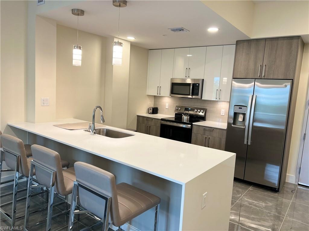 Kitchen with sink, appliances with stainless steel finishes, white cabinetry, a kitchen bar, and dark brown cabinetry