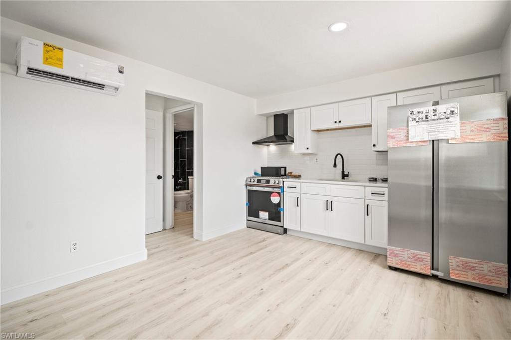 Kitchen featuring stainless steel appliances, wall chimney exhaust hood, a wall mounted AC, light wood-style flooring, and light countertops