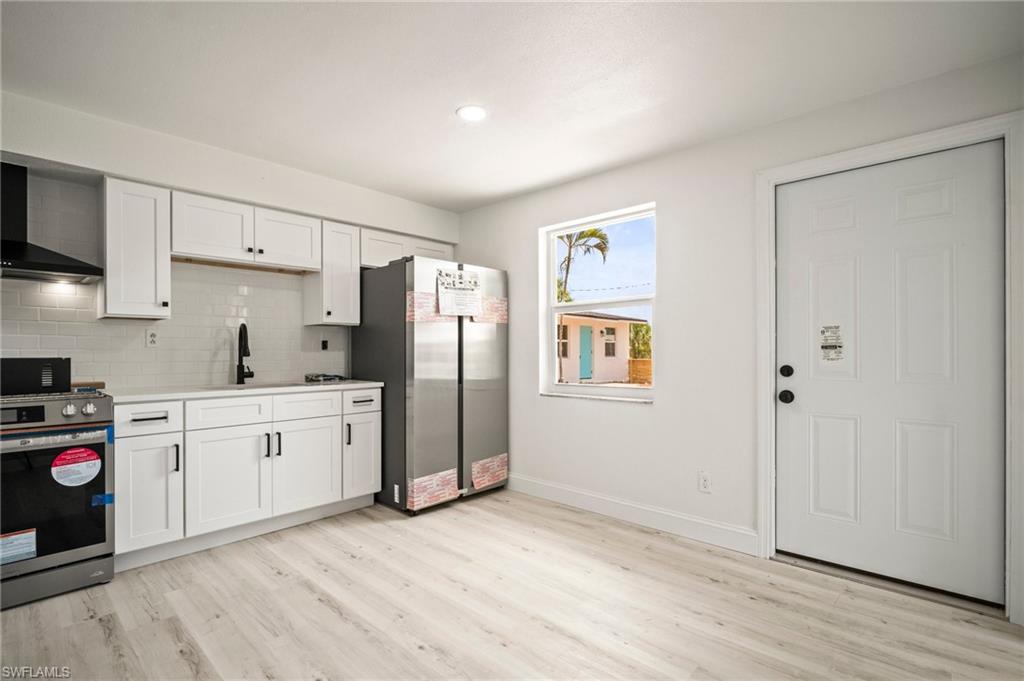 Kitchen featuring appliances with stainless steel finishes, light wood-style flooring, decorative backsplash, white cabinets, and recessed lighting