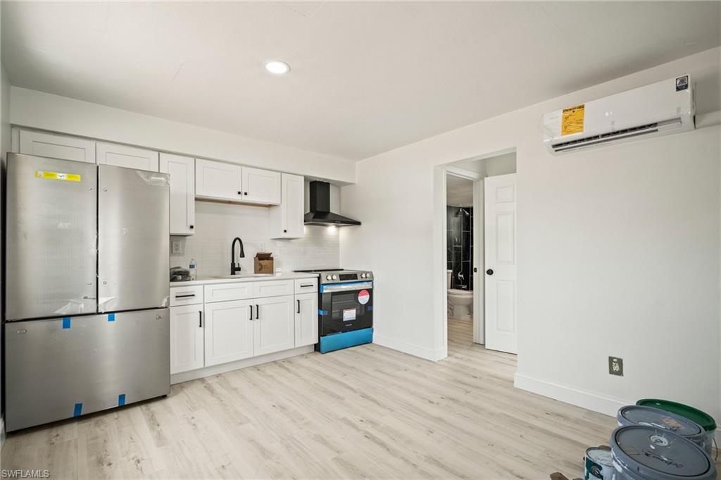 Kitchen featuring stainless steel appliances, a wall mounted air conditioner, wall chimney range hood, light wood-type flooring, and backsplash