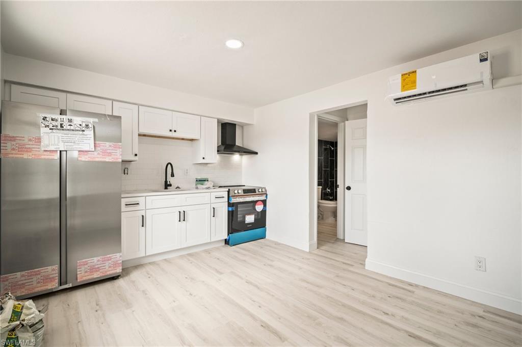 Kitchen with appliances with stainless steel finishes, wall chimney exhaust hood, an AC wall unit, light countertops, and light wood-style floors