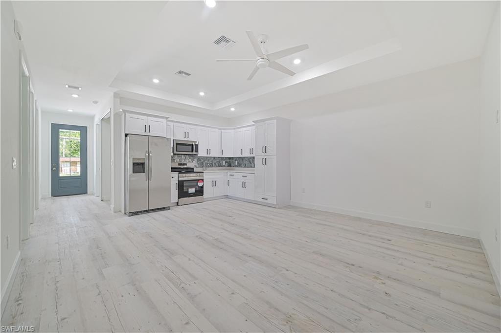 Unfurnished living room featuring a raised ceiling, light hardwood / wood-style floors, and ceiling fan