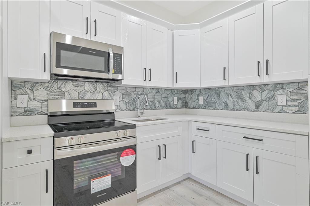 Kitchen featuring light hardwood / wood-style flooring, stainless steel appliances, white cabinets, and tasteful backsplash