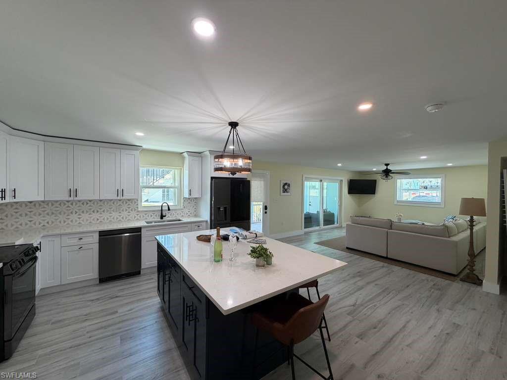 Contemporary kitchen featuring white cabinetry, a patterned tile backsplash, stainless steel appliances, and a dark island with a light-colored countertop