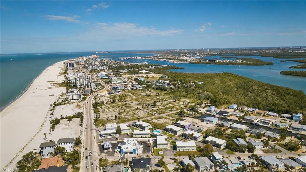 Coastal landscape featuring expansive sandy beaches, a linear road, residential properties, and dense natural foliage bordering waterways