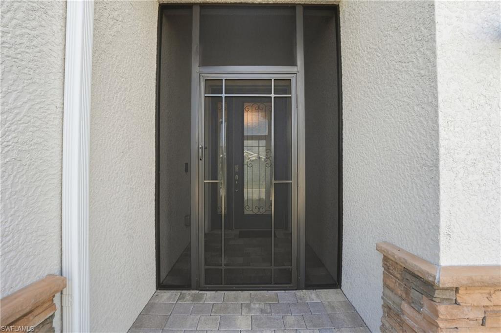 Entryway with gray paver flooring, textured stucco exterior, stacked stone accents, and a full-view screen enclosure