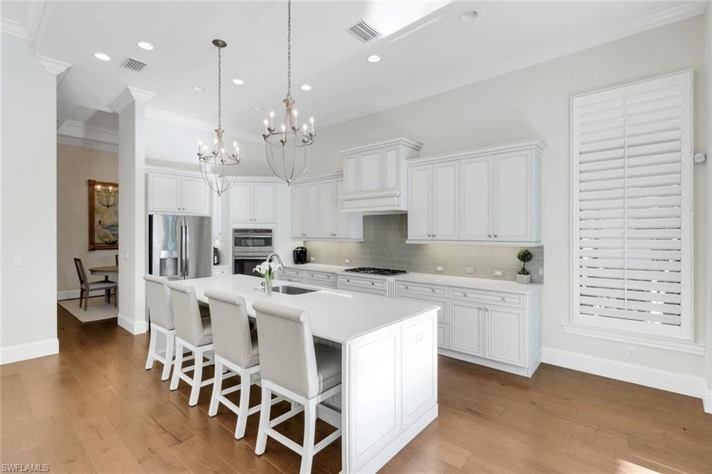 Kitchen featuring a white cabinetry, crown molding, decorative light fixtures, and a kitchen island with sink