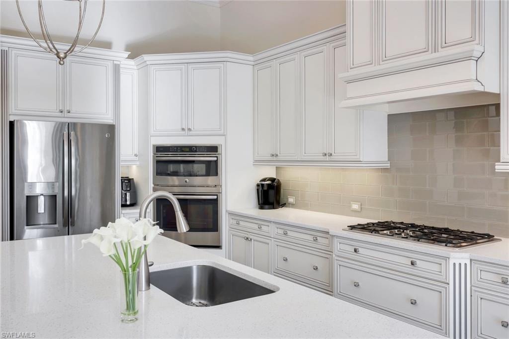 Kitchen featuring stainless steel appliances, white cabinets, quartz countertops, decorative backsplash, and custom range hood