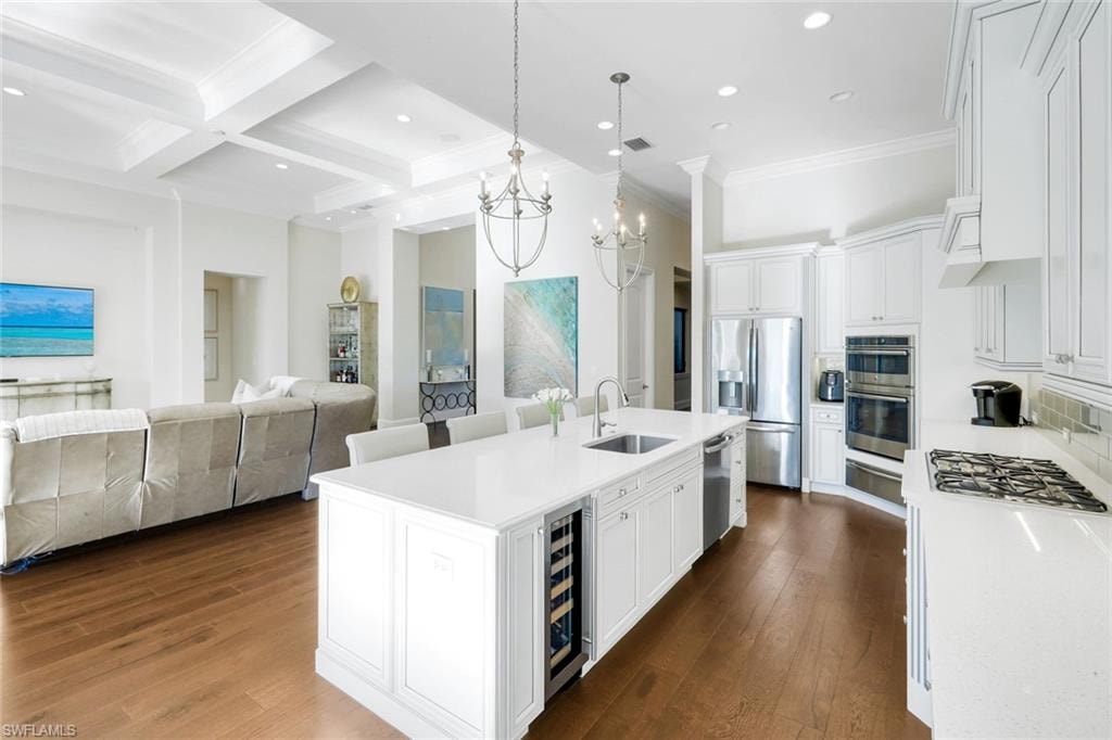 Kitchen with white cabinets, coffered ceiling, open floor plan, hanging light fixtures, and appliances with stainless steel finishes