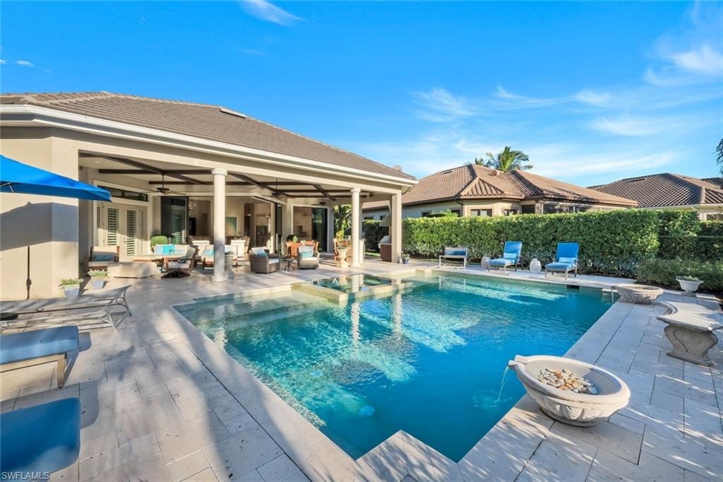 View of swimming pool featuring a patio area, a pool with connected hot tub, and an outdoor living space with a fire pit