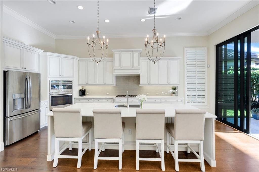 Kitchen featuring stainless steel appliances, a breakfast bar area, crown molding, white cabinets, and an island with sink