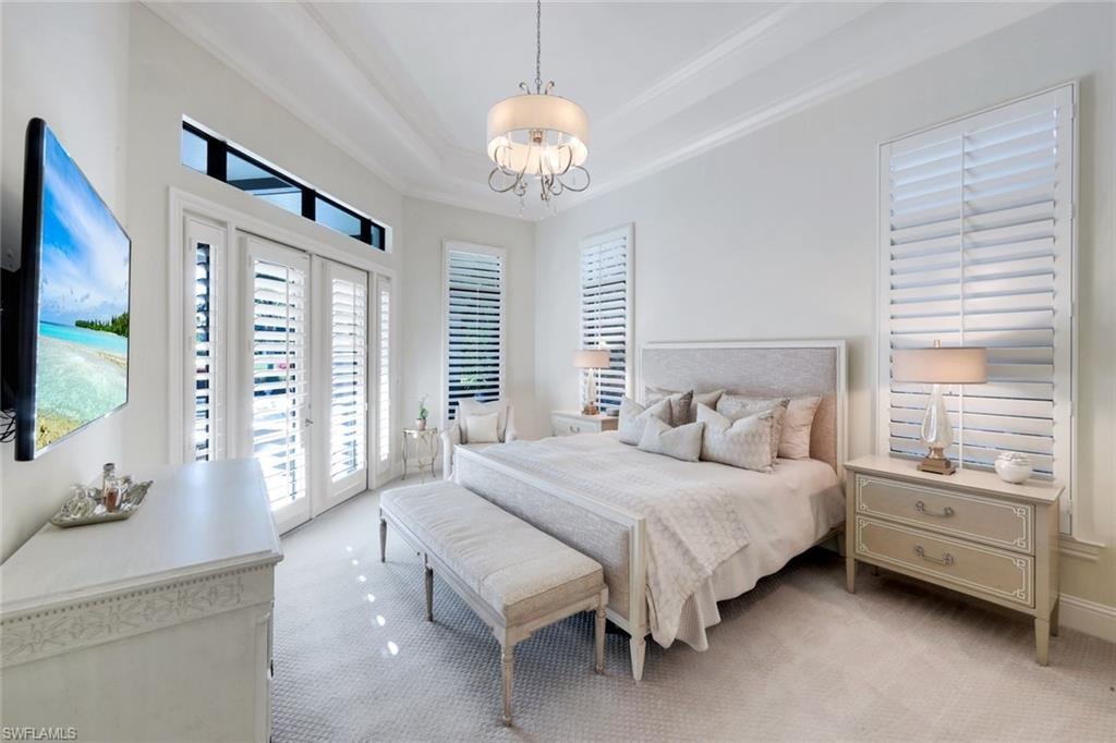 King Bedroom featuring access to outside, carpet flooring, a tray ceiling, a chandelier, and crown molding