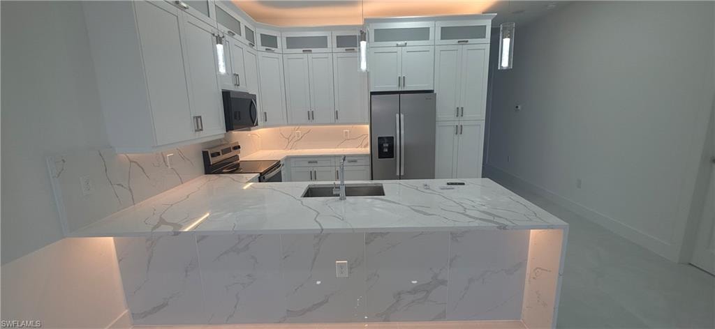 Kitchen featuring a large central island with undermount sink, white cabinetry with upper glass-front accents, stainless steel appliances, and integrated under-cabinet lighting