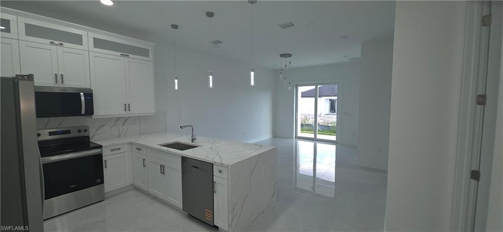 Modern kitchen featuring a waterfall-edge island with integrated sink, white cabinetry with upper glass accents, stainless steel appliances, and large format tile flooring