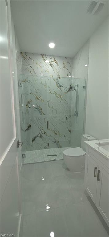 Spacious bathroom featuring a glass-enclosed shower with white and gold-veined tile, a white toilet, and a vanity with white cabinetry and a light-colored countertop