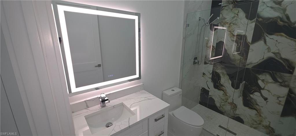 Bathroom featuring a contemporary vanity with a white countertop and integrated sink, an illuminated mirror, and a glass-enclosed shower with large format marble-look tile